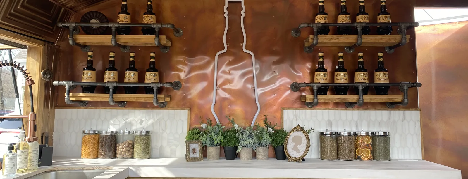 The finished interior of a mobile bar build: pressed tin ceiling, bottles on pipe shelving and a copper back wall